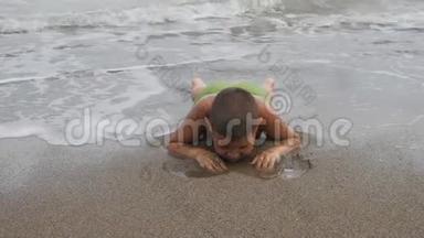 孩子躺在<strong>海浪</strong>中的沙岸上。 男孩在海滩上划沙。 孩子洗了<strong>海浪</strong>。